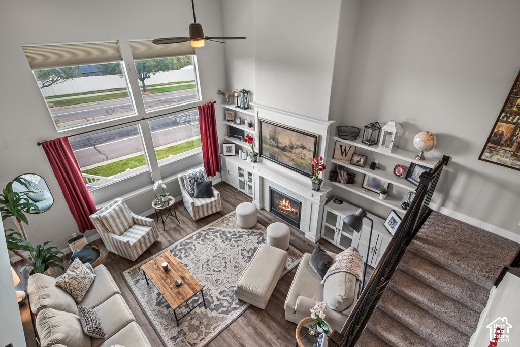 Two-story living area featuring a fireplace with white mantel, built-in shelving, wood-finish flooring, and a ceiling fan