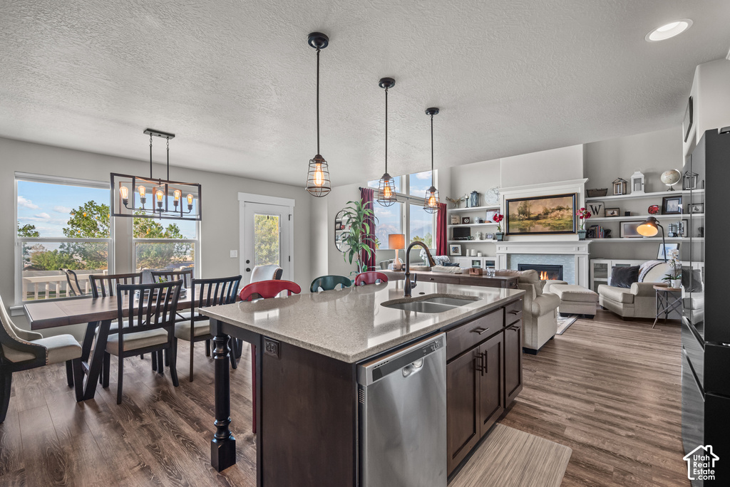 Open-concept living space with wood-finish flooring, a kitchen island with integrated sink, pendant lighting, and a dining area with a linear chandelier