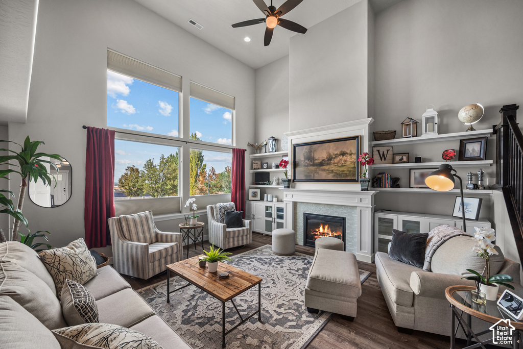 High ceilings featuring large windows with window treatments, a fireplace with a light-colored tile surround and white mantel, built-in shelving, and wood-finish flooring