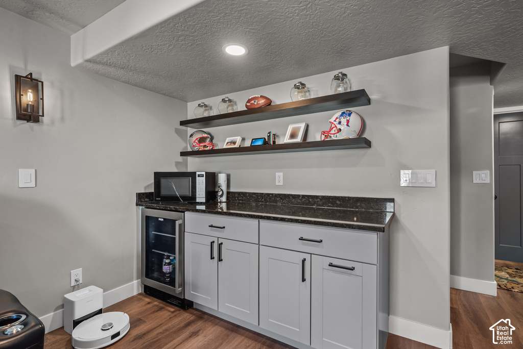 Built-in refreshment station featuring a dark granite countertop, light gray shaker-style cabinetry with matte black hardware, and integrated beverage refrigerator