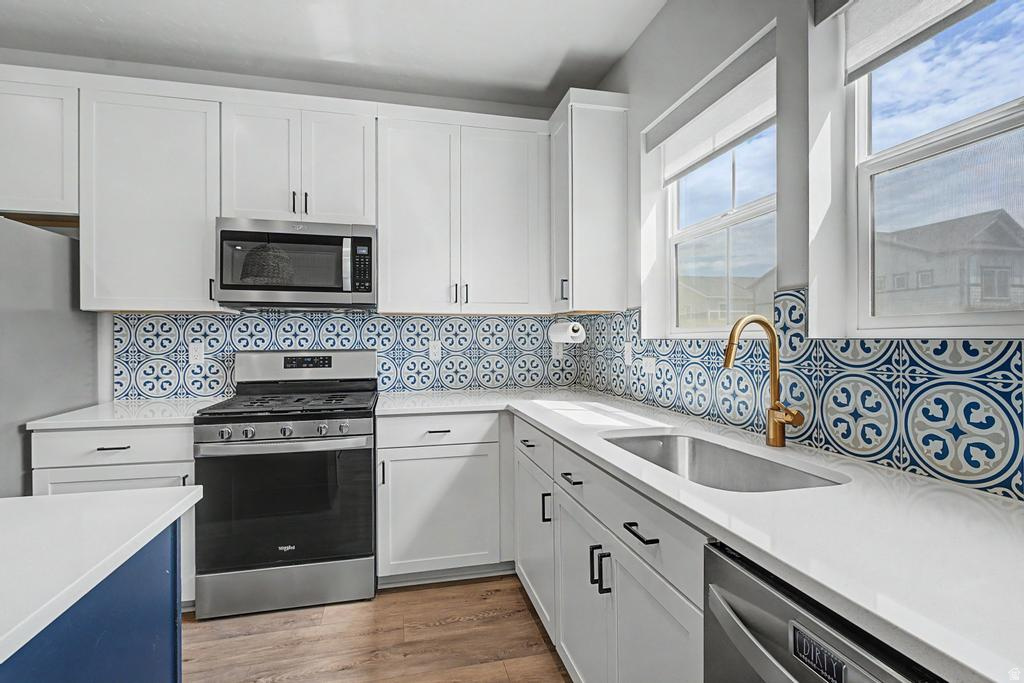 Contemporary kitchen featuring white cabinetry, stainless steel appliances, a patterned tile backsplash, and light-colored countertops
