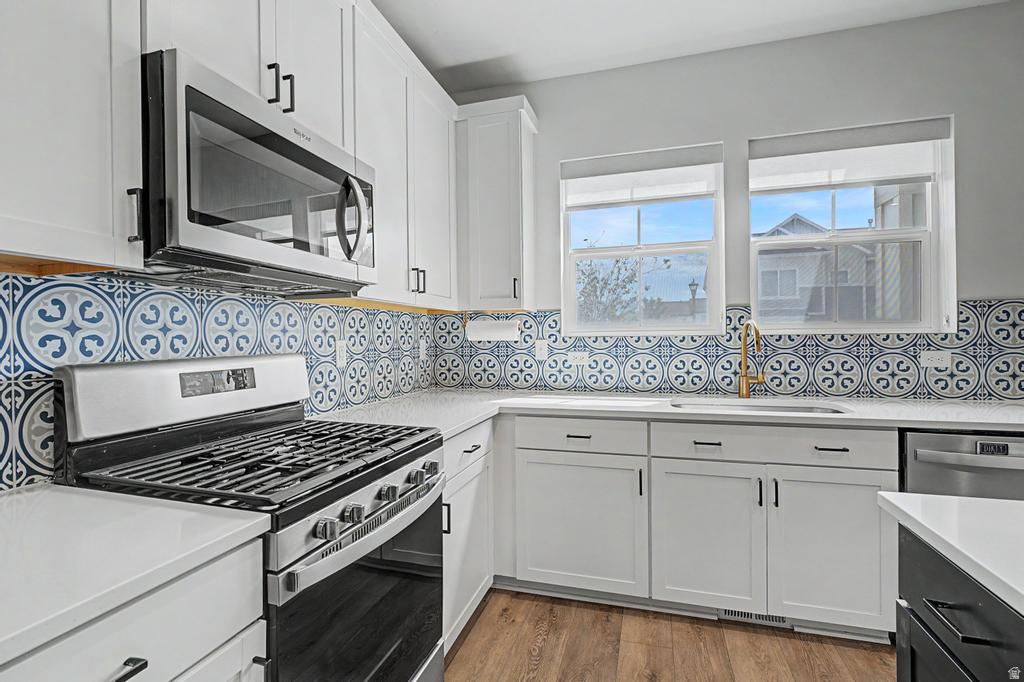 Kitchen featuring white cabinetry, patterned tile backsplash, stainless steel appliances, white countertops, and wood-finish flooring