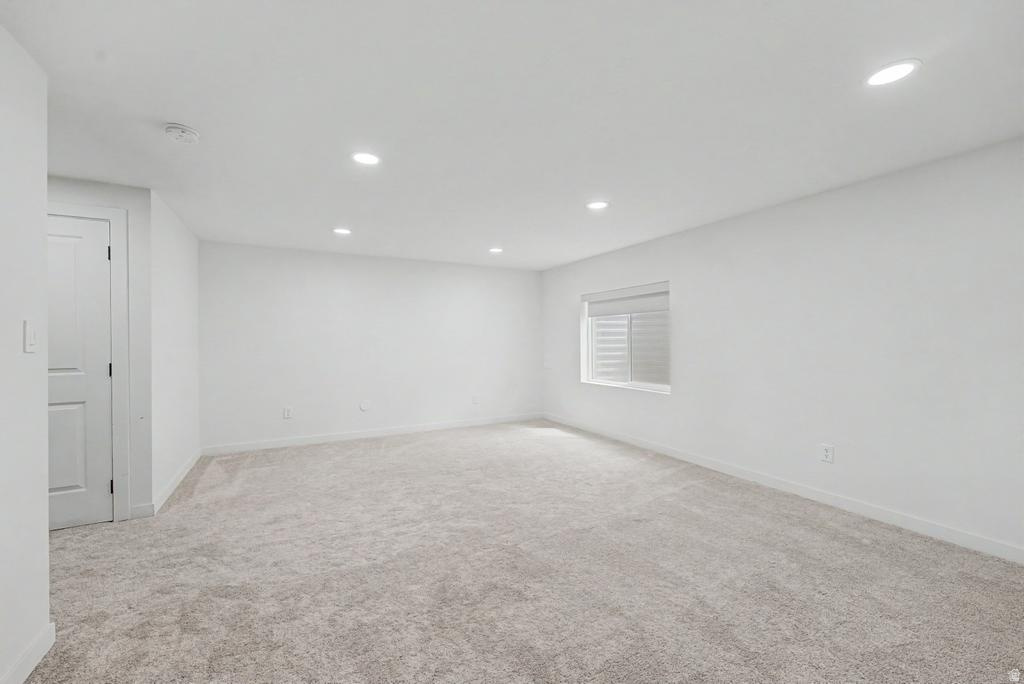 Spacious room featuring light-colored carpeting, white painted walls, recessed ceiling lighting, and a single window with horizontal blinds