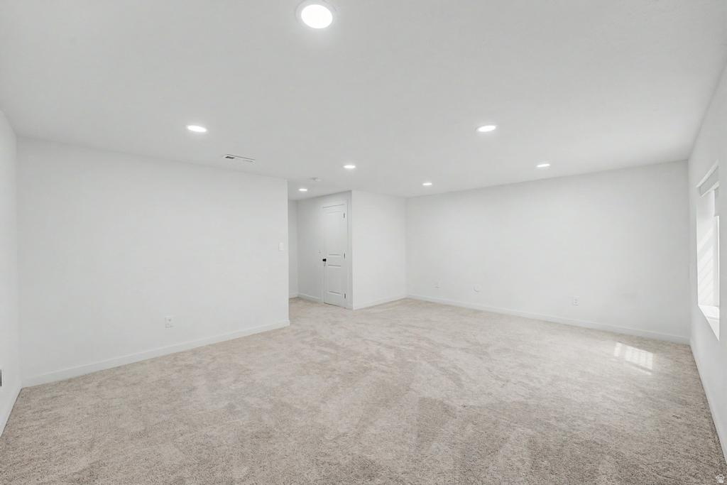 Spacious room with recessed lighting, light-toned carpet flooring, white walls, and a single window offering ambient light