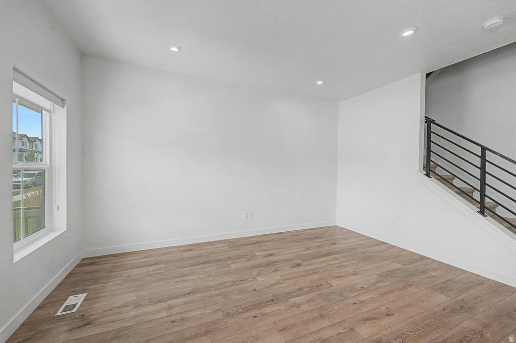 Spacious room featuring wood-finish flooring, recessed lighting, a large window, and a contemporary staircase with metal railings