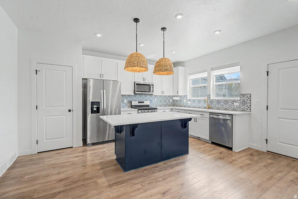 Kitchen featuring a central island with a white countertop and blue base, stainless steel appliances, patterned backsplash, wood-finish flooring, and recessed lighting