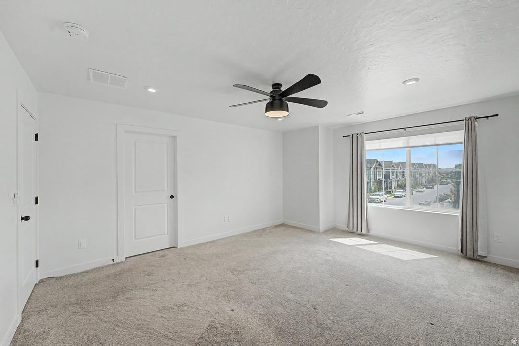 Spacious room featuring neutral carpeting, a large window with roller shades, and a modern ceiling fan with integrated lighting