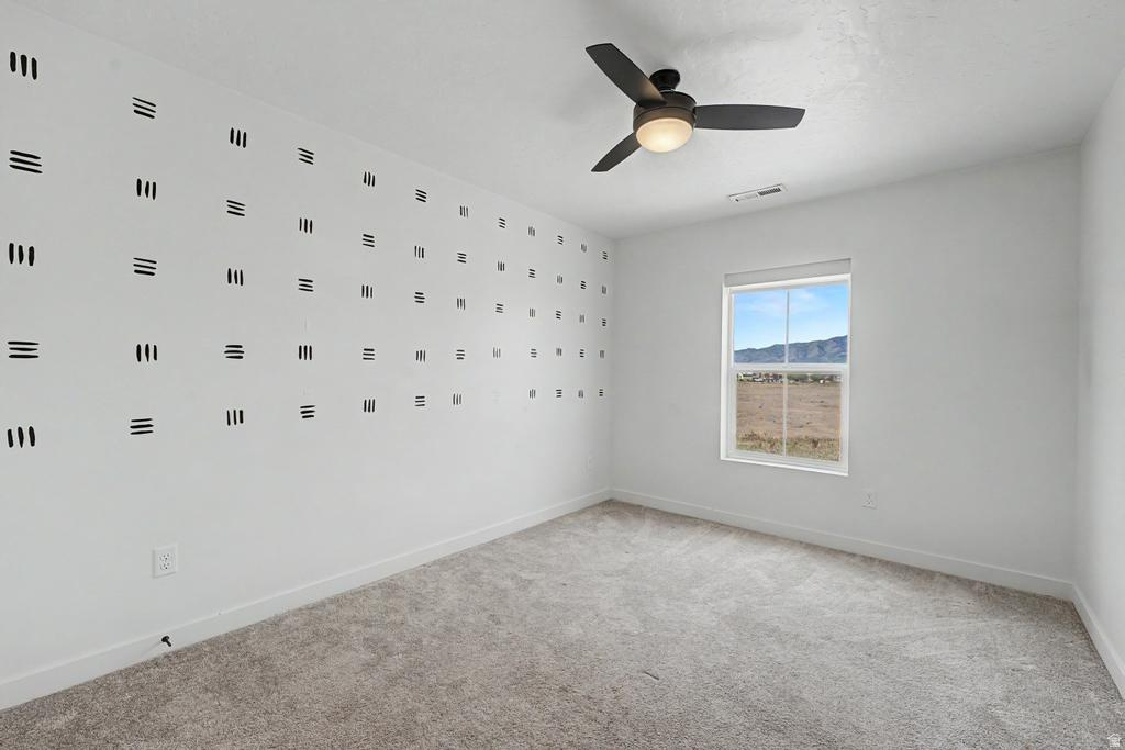 Room featuring light gray carpet flooring, a single window with a mountain backdrop, a ceiling fan with integrated lighting, and a white wall with a geometric pattern
