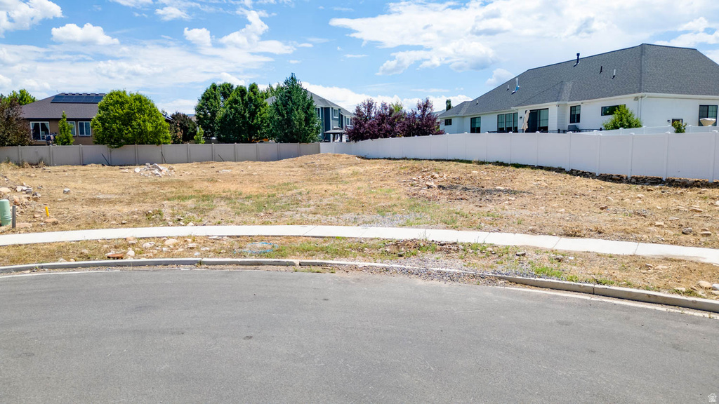 Vacant land parcel featuring a paved street, concrete sidewalk, and surrounding white vinyl fencing