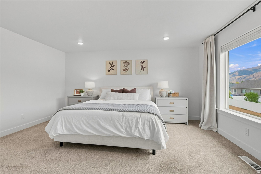 Spacious bedroom featuring light neutral carpet, recessed lighting, and a large window with mountain scenery