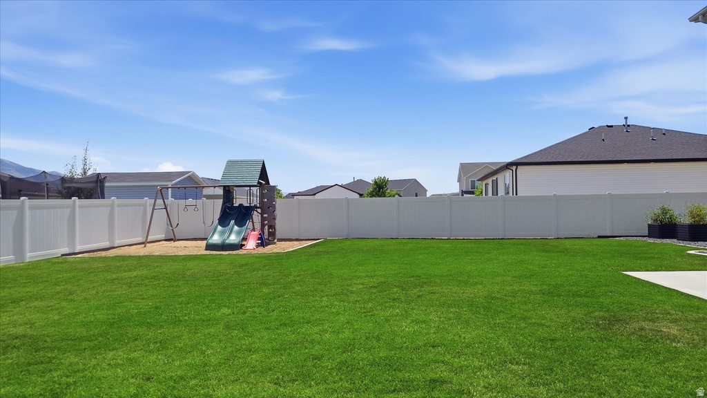 Expansive fenced backyard featuring a substantial lawn area, a built-in play structure with slides, and a patio area