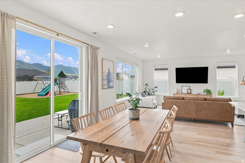 Spacious open-concept living area featuring light wood-finish flooring, recessed lighting, and large sliding glass doors opening to a fenced backyard with a patio