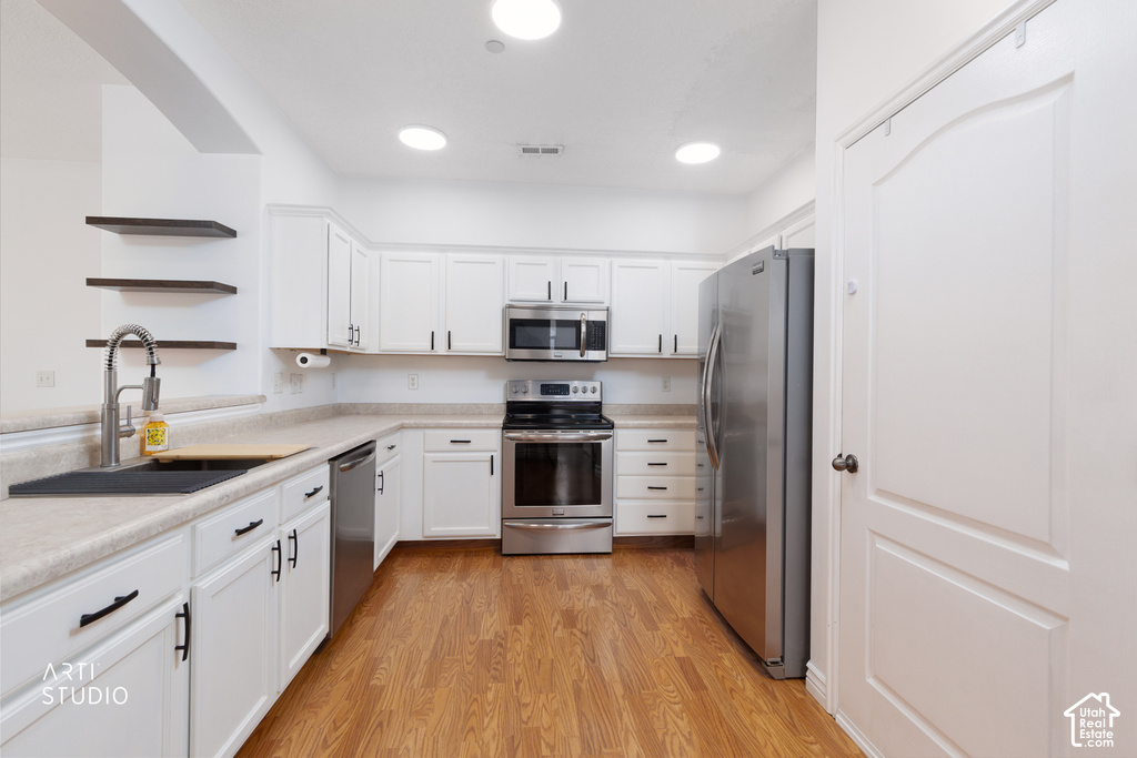 Kitchen featuring white cabinetry, stainless steel appliances, wood-finish flooring, light-toned countertops, and open shelving