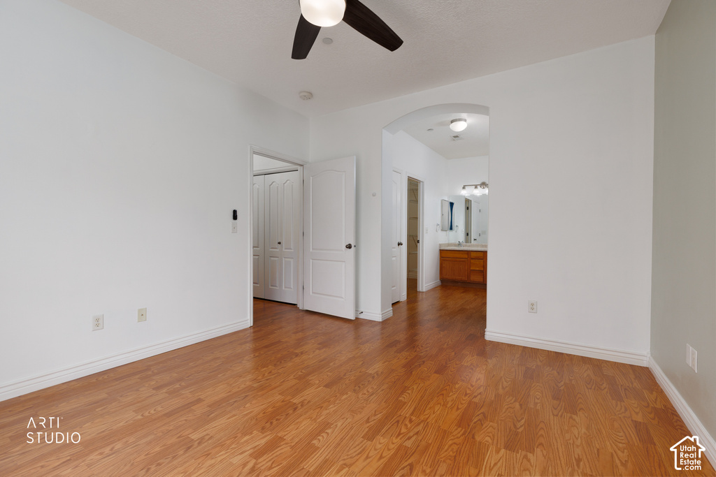 Spacious room featuring wood-finish flooring, a ceiling fan, and access to a bathroom with a double vanity
