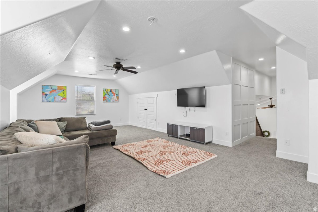 Spacious carpeted room featuring a ceiling fan, recessed lighting, and sloped ceilings