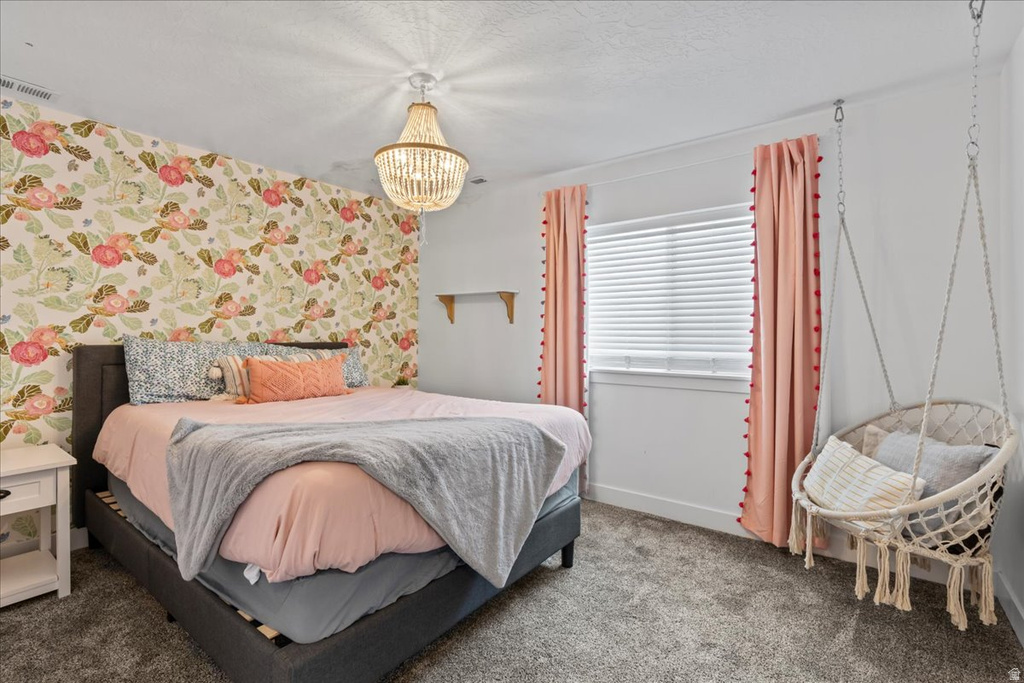 Bedroom featuring a floral accent wall, plush carpeting, a window with horizontal blinds, and a beaded chandelier