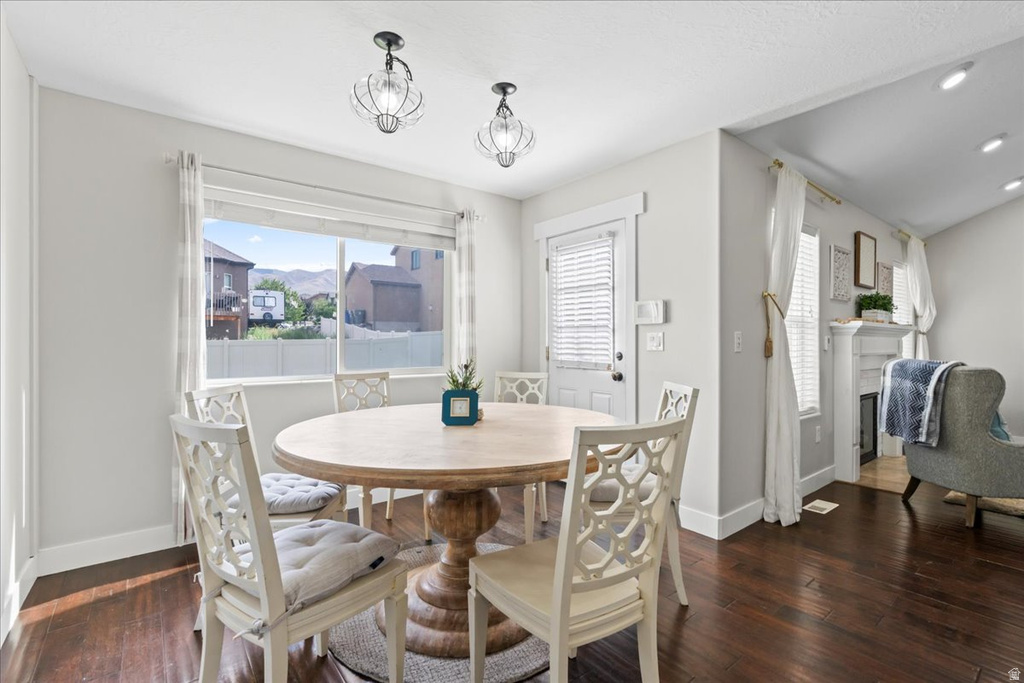 Dining area featuring dark wood-finish flooring, a large window, a ceiling-mounted light fixture, and a built-in fireplace with a mantel
