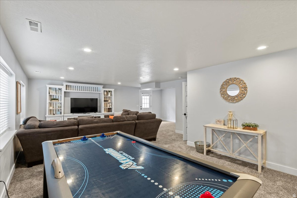 Spacious entertainment area featuring recessed lighting, light gray walls, and plush carpet flooring