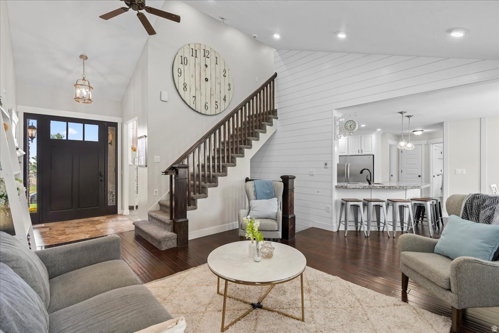 Vaulted ceiling interior featuring dark wood-finish flooring, a dark wood staircase with carpeted treads, a dark paneled front door with upper lites, and a kitchen pass-through with counter seating