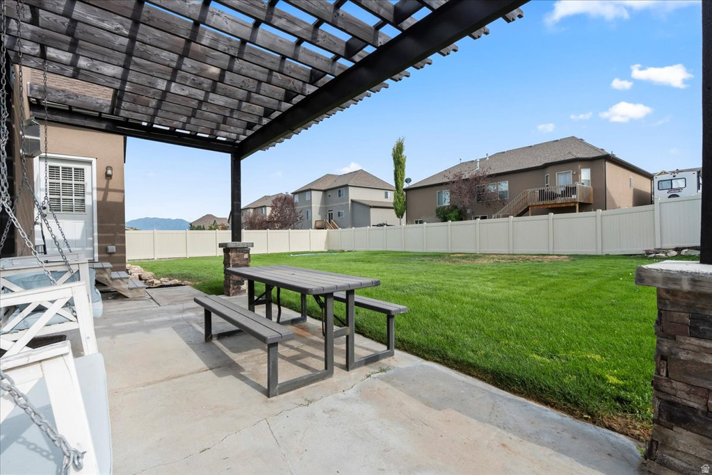 Expansive backyard featuring a pergola-covered patio, concrete slab, and a vibrant green lawn