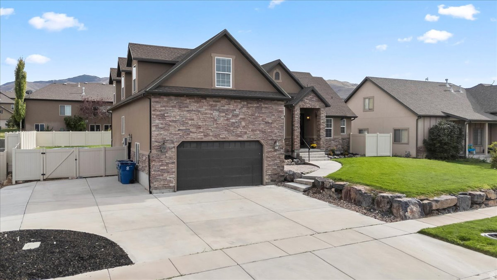 Contemporary stucco and stone-veneer exterior featuring an attached two-car garage, concrete driveway, and a manicured front lawn with rock retaining walls
