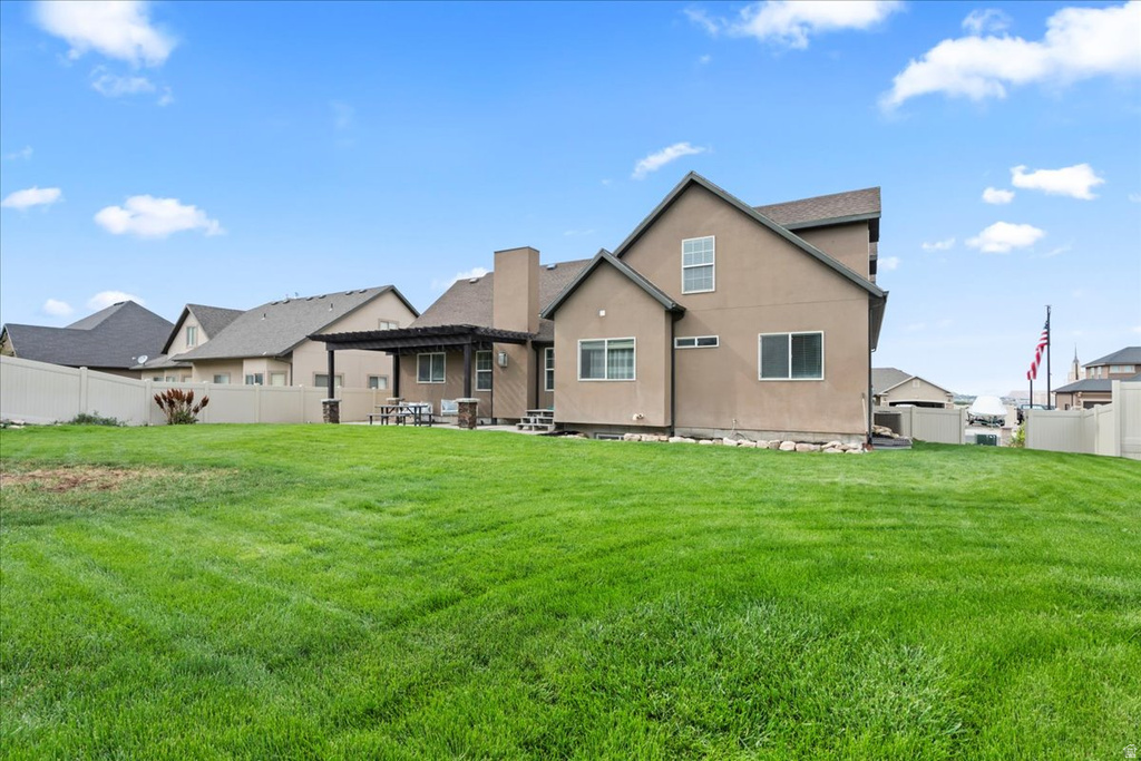 Expansive backyard featuring a manicured lawn, a stucco exterior, a covered patio with a dark wood pergola, and a light-colored privacy fence