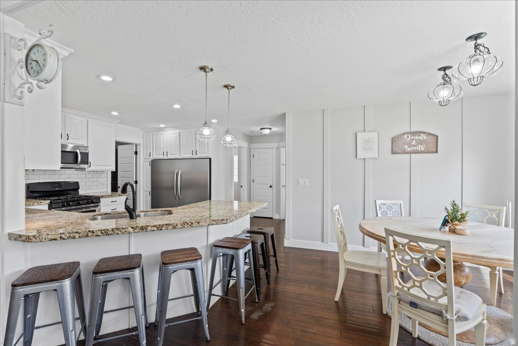 Kitchen and dining area featuring dark wood-finish flooring, white cabinetry, a granite-finish island with seating, a subway tile backsplash, and stainless steel appliances