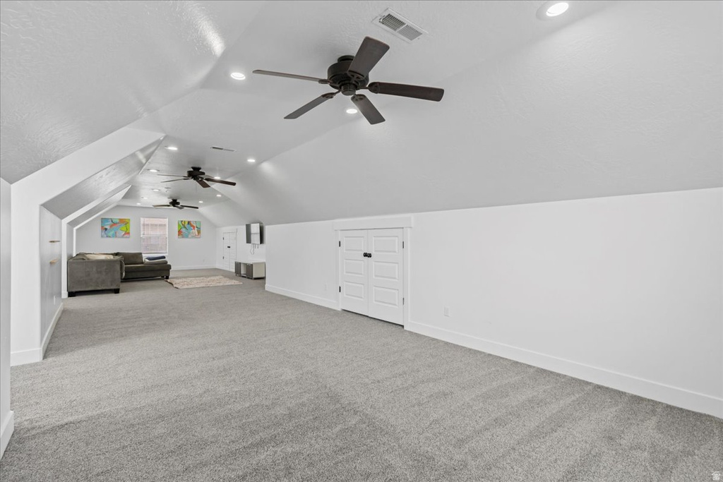Spacious bonus room featuring vaulted ceilings, recessed lighting, gray carpet, multiple ceiling fans, and built-in double-door storage