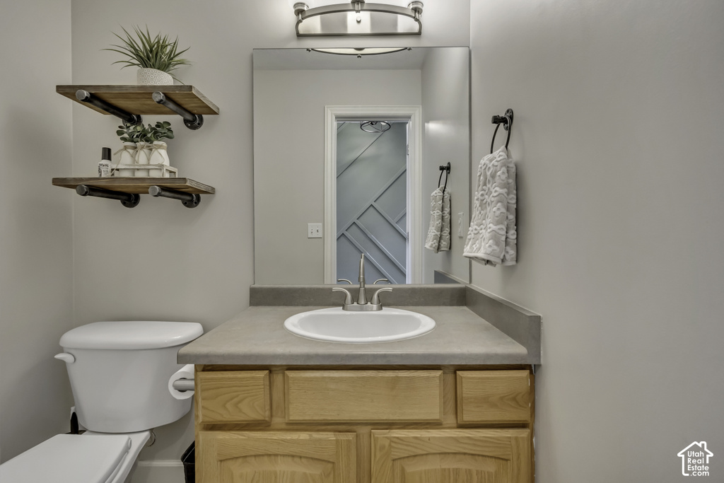 Bathroom vanity featuring a light wood-finish cabinet with a solid surface countertop, an undermount sink, and a wall-mounted mirror