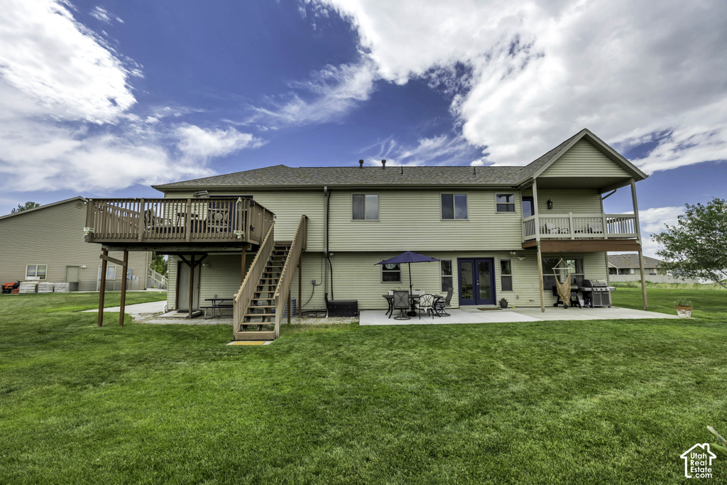 Expansive backyard featuring a manicured lawn, a large elevated wood deck with stairs, a concrete patio, and a covered second-story balcony