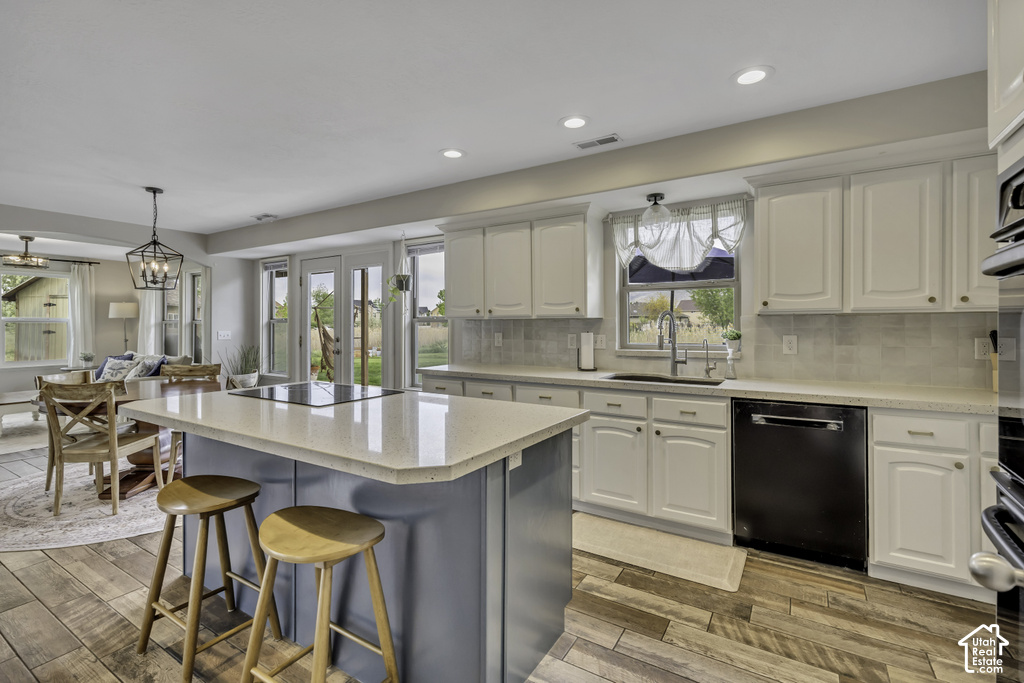 Kitchen featuring a central island with a built-in cooktop, light-toned countertops, white cabinetry with gold-finish hardware, a stainless steel sink, and wood-finish flooring