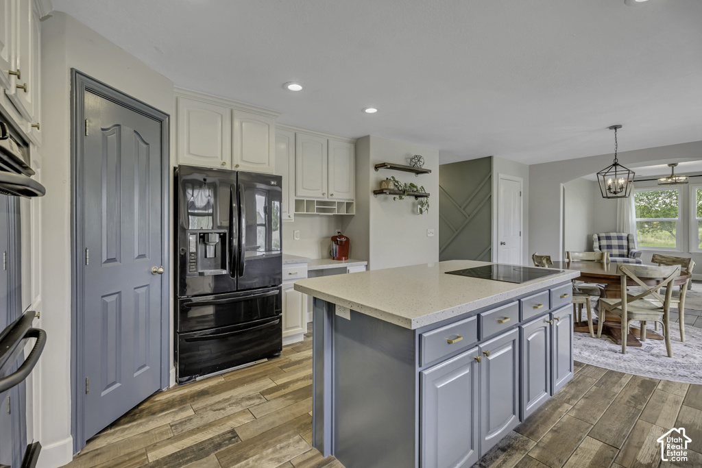 Gourmet kitchen with wood-finish flooring, white cabinetry, a built-in black refrigerator, and a kitchen island featuring blue-painted cabinetry, a light-colored countertop, and an integrated cooktop