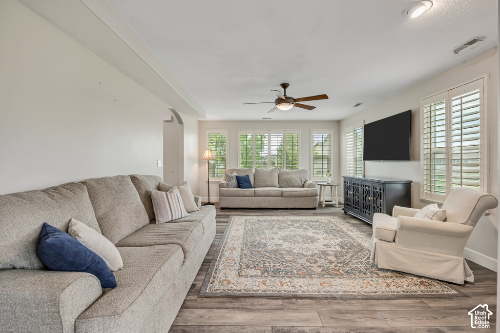 Living area featuring wood-finish flooring, a ceiling fan with integrated lighting, recessed lighting, and multiple windows with plantation shutters