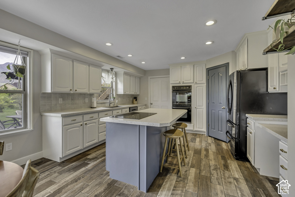 Spacious kitchen featuring an expansive island with seating, white shaker-style cabinetry, light-toned countertops, wood-finish flooring, and a subway tile backsplash