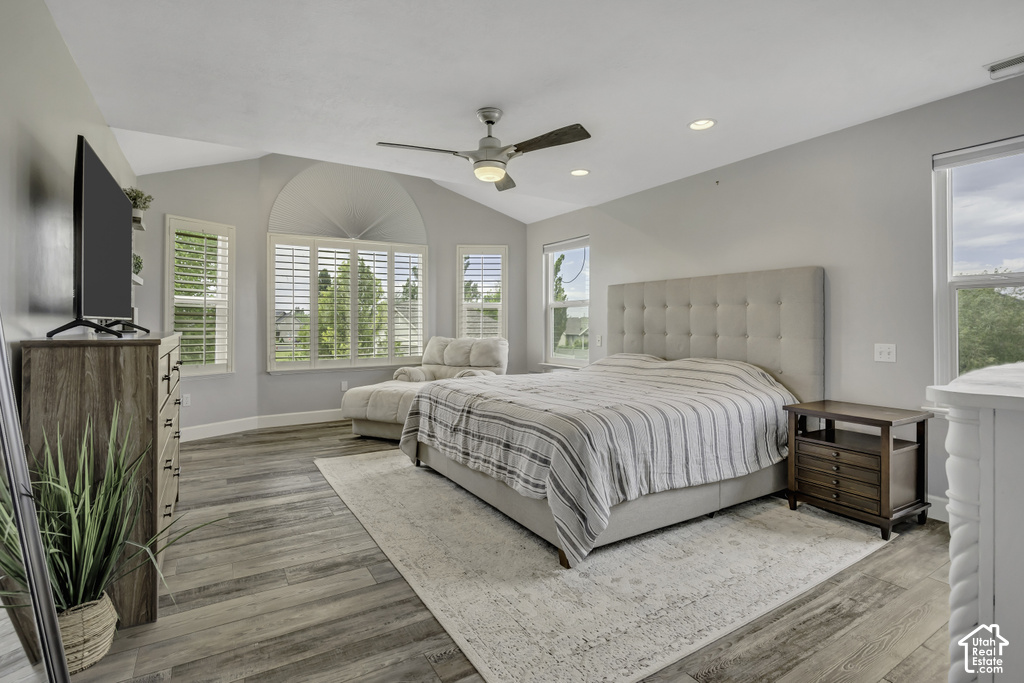 Spacious room featuring vaulted ceilings, wood-finish flooring, recessed lighting, a ceiling fan, and multiple windows with plantation shutters