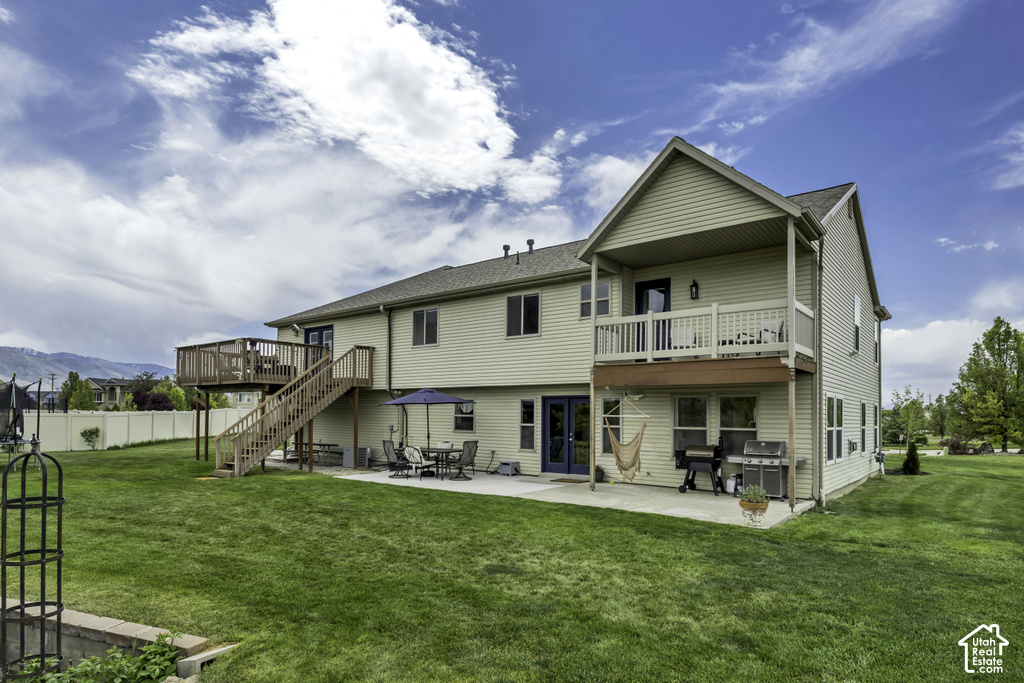 Expansive backyard featuring a large green lawn, two-story siding exterior, multi-level deck, ground-level patio, and a white privacy fence