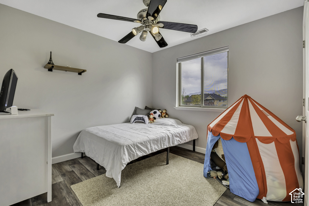 Bedroom featuring wood-finish flooring, a ceiling fan with integrated lighting, and a single window with a mountain backdrop