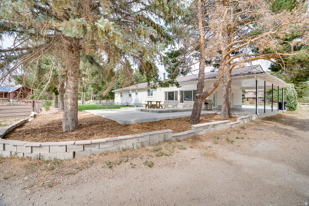 Rear exterior featuring a concrete patio, a covered concrete patio, mature trees, and a retaining wall