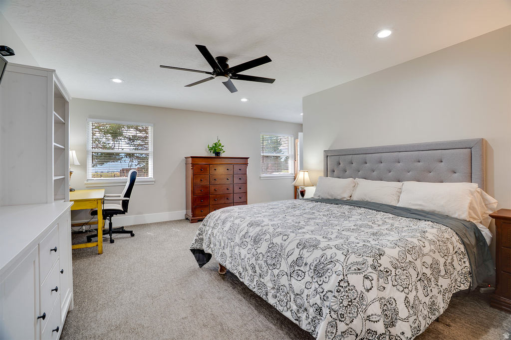Spacious bedroom featuring light neutral wall tones, carpeted flooring, a ceiling fan, recessed lighting, and multiple windows with blinds