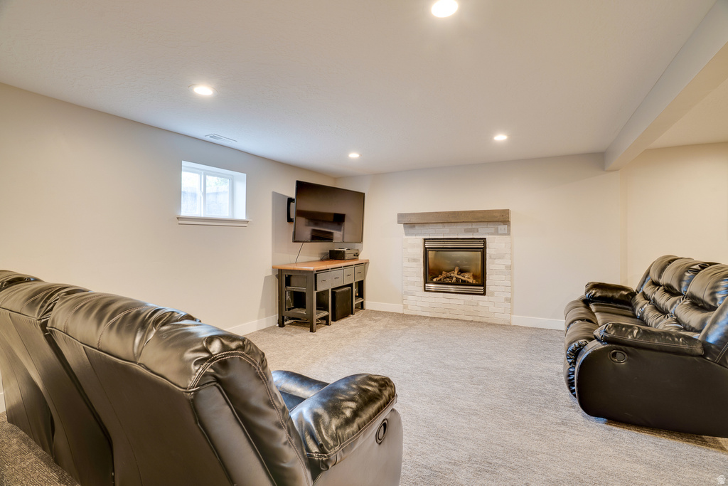 Carpeted recreation room featuring a modern fireplace with a light-toned brick surround and a wood-finish mantel
