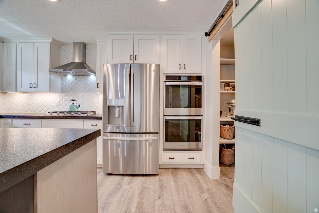 Modern kitchen featuring white shaker cabinetry, stainless steel appliances, dark countertops, and wood-finish flooring
