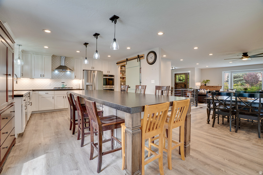 Spacious kitchen featuring a large island with seating, light wood-finish flooring, white cabinetry, stainless steel appliances, and recessed lighting