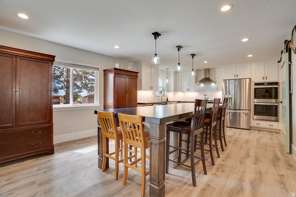 Spacious kitchen featuring a large central island with seating, pendant lighting, stainless steel appliances, white cabinetry, and wood-finish flooring