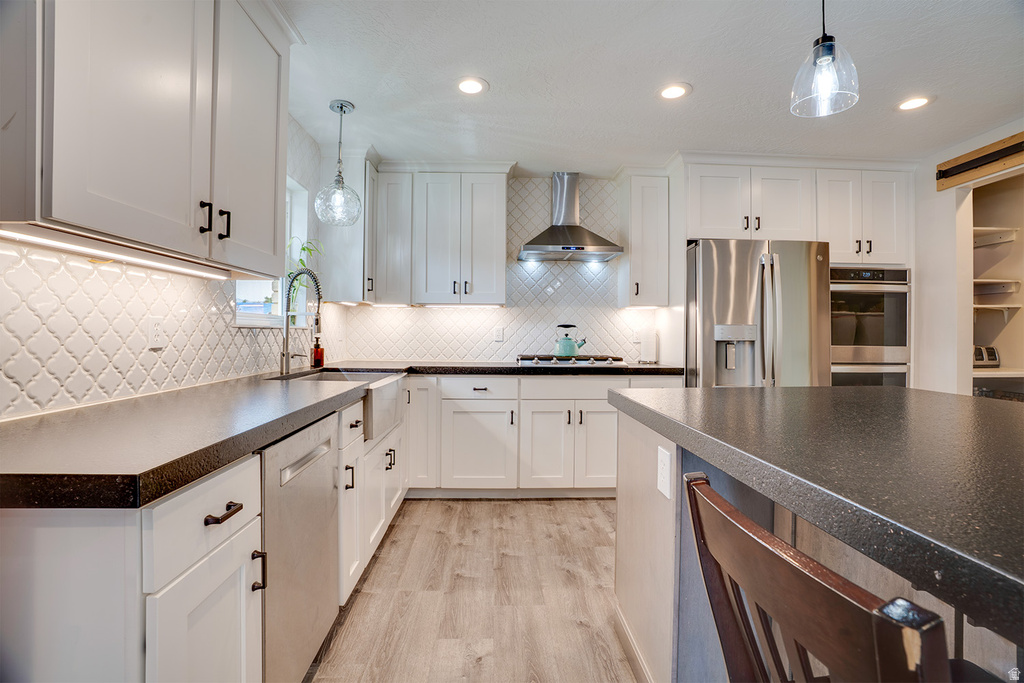 Kitchen featuring white shaker cabinetry, dark countertops, a farmhouse sink, stainless steel appliances, and wood-finish flooring