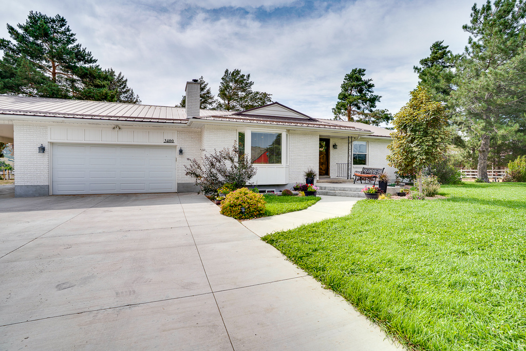 White brick exterior featuring a white metal roof, attached two-car garage, and concrete driveway