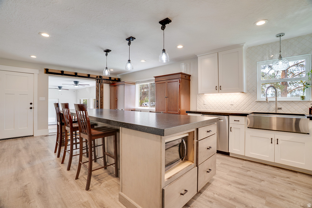 Spacious kitchen featuring a large island with built-in microwave, light wood-finish flooring, white shaker cabinetry with dark hardware, a stainless steel apron sink, and a white diagonal tile backsplash