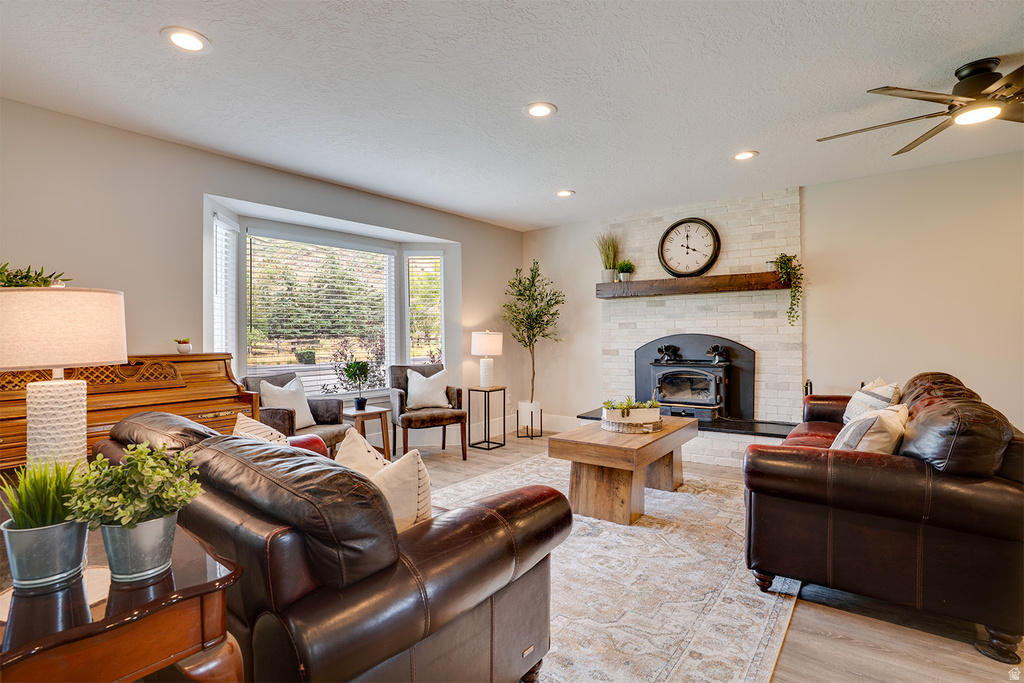 Living area featuring a white brick fireplace with a wood mantle, a wood-burning stove, recessed lighting, and a ceiling fan
