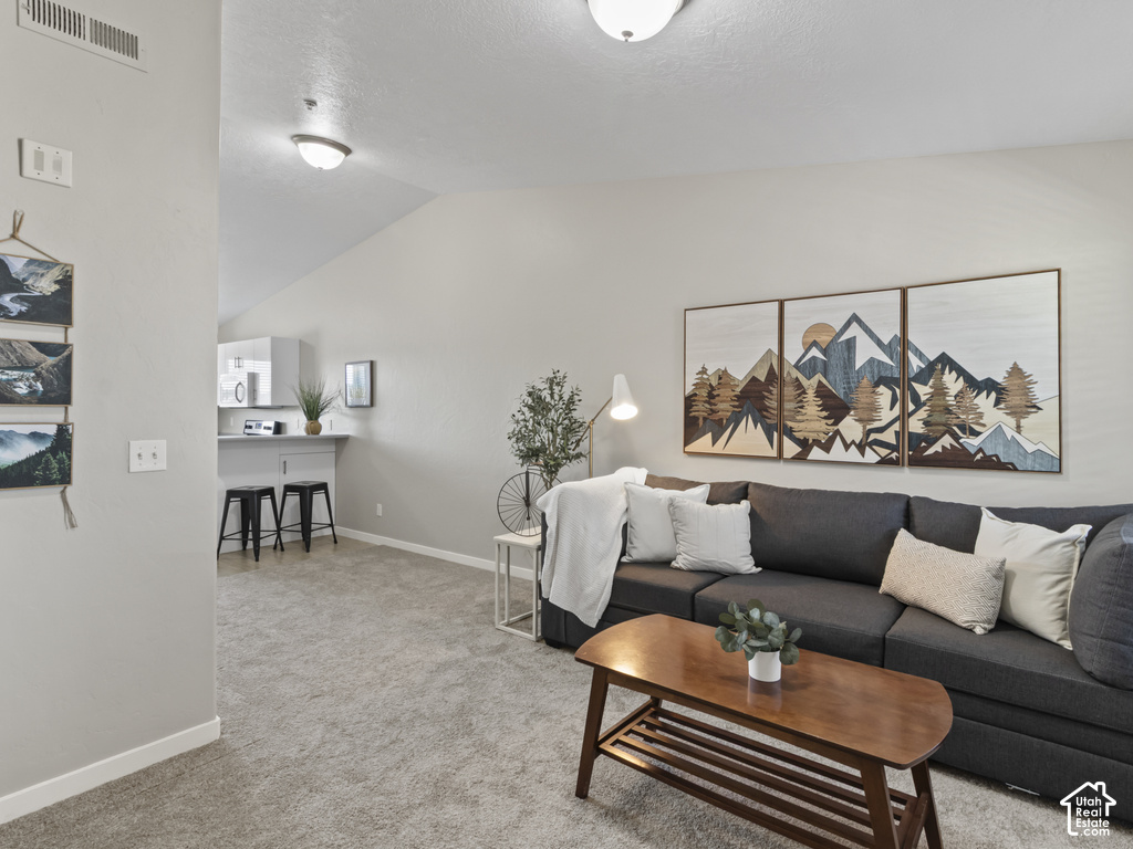 Open-concept living space featuring vaulted ceilings, neutral wall tones, and plush carpeting