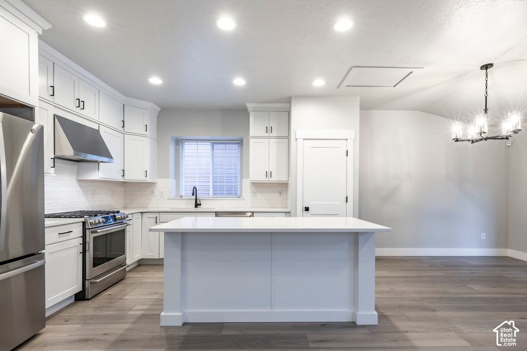 Chef's kitchen featuring white shaker cabinetry, stainless steel appliances including a gas range and range hood, quartz countertops, and a large waterfall-edge island with paneled base