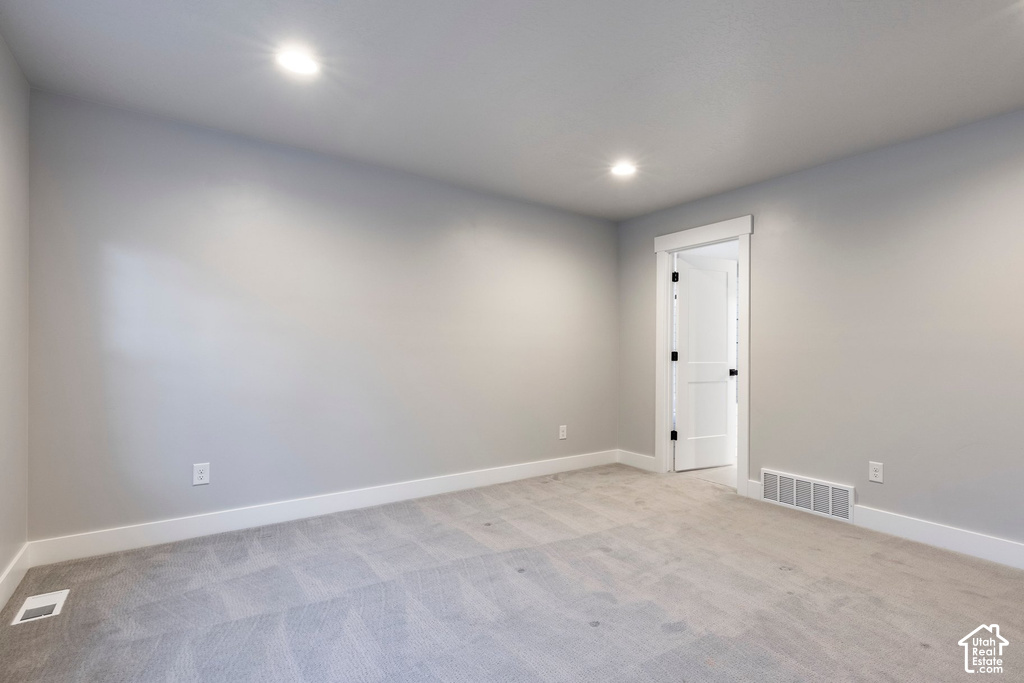 Spacious room featuring light gray carpeting, neutral wall finishes, bright recessed lighting, white baseboards, and a white door with dark hardware